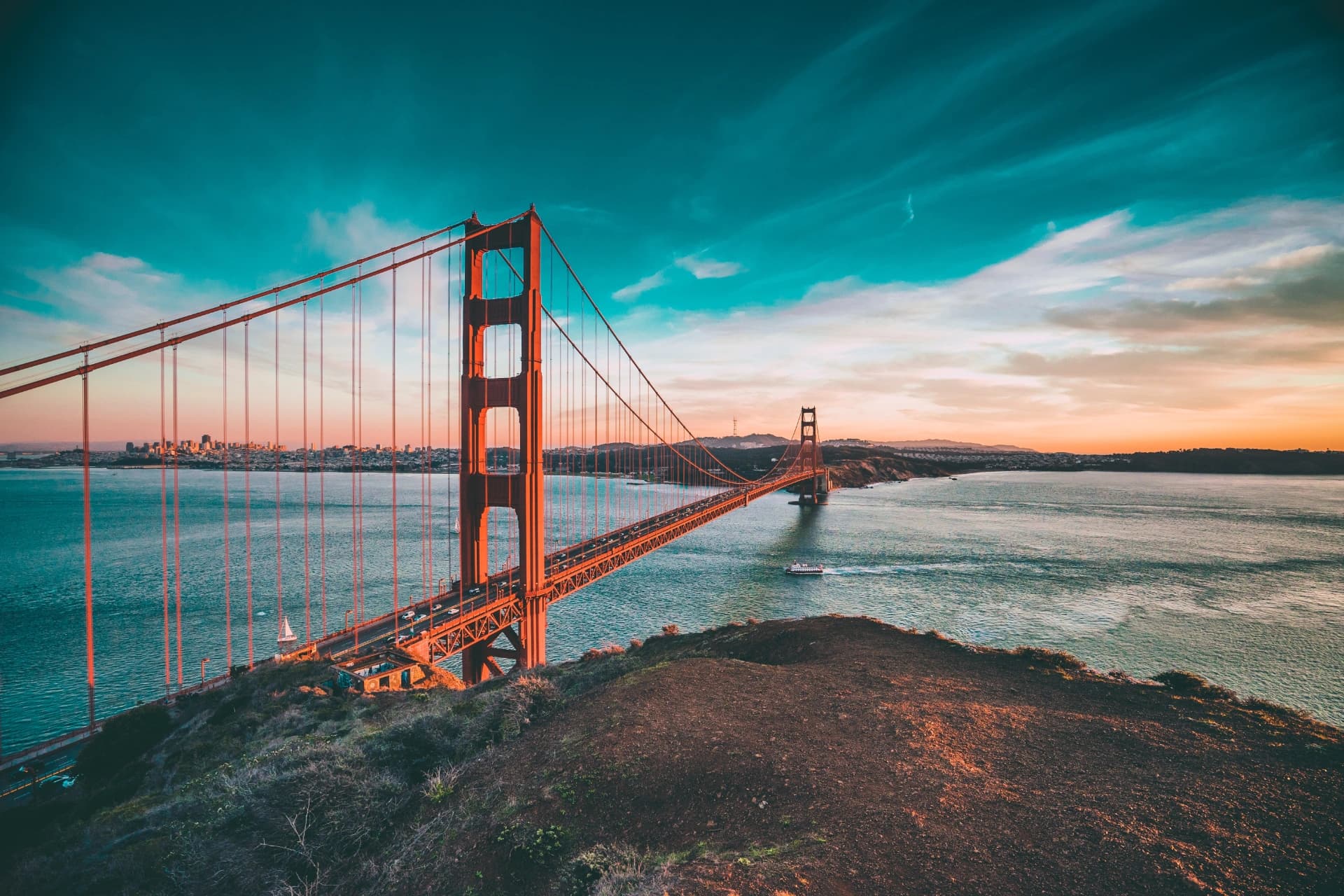 The Golden Gate Bridge at sunset seen from a hillside in the Marin Headlands, with the San Francisco skyline across the bay