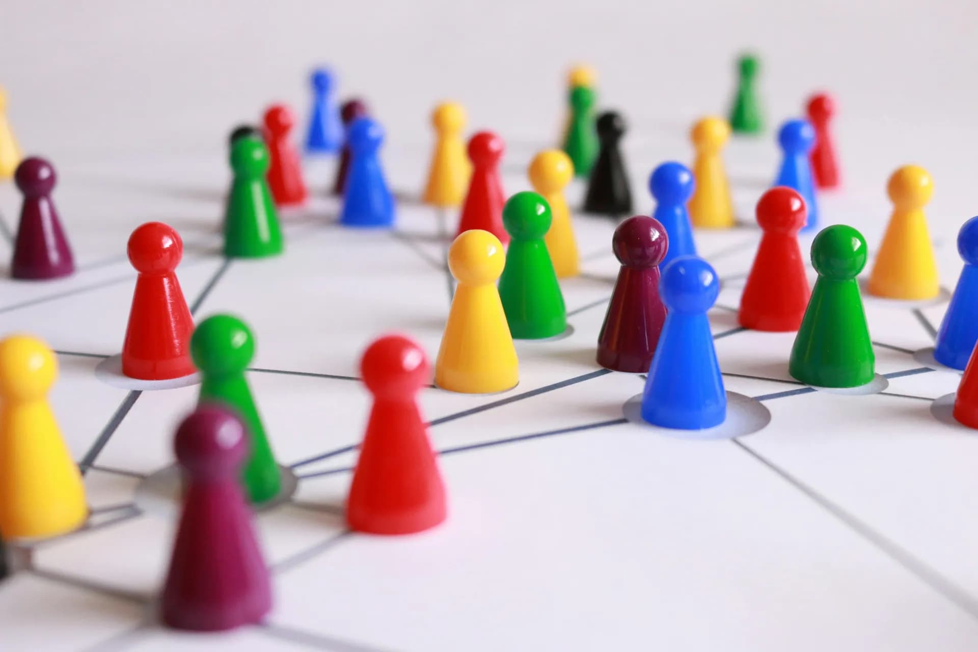 Colorful game pawns standing on a white board, connected to one another by a web of thin gray lines like nodes in a network