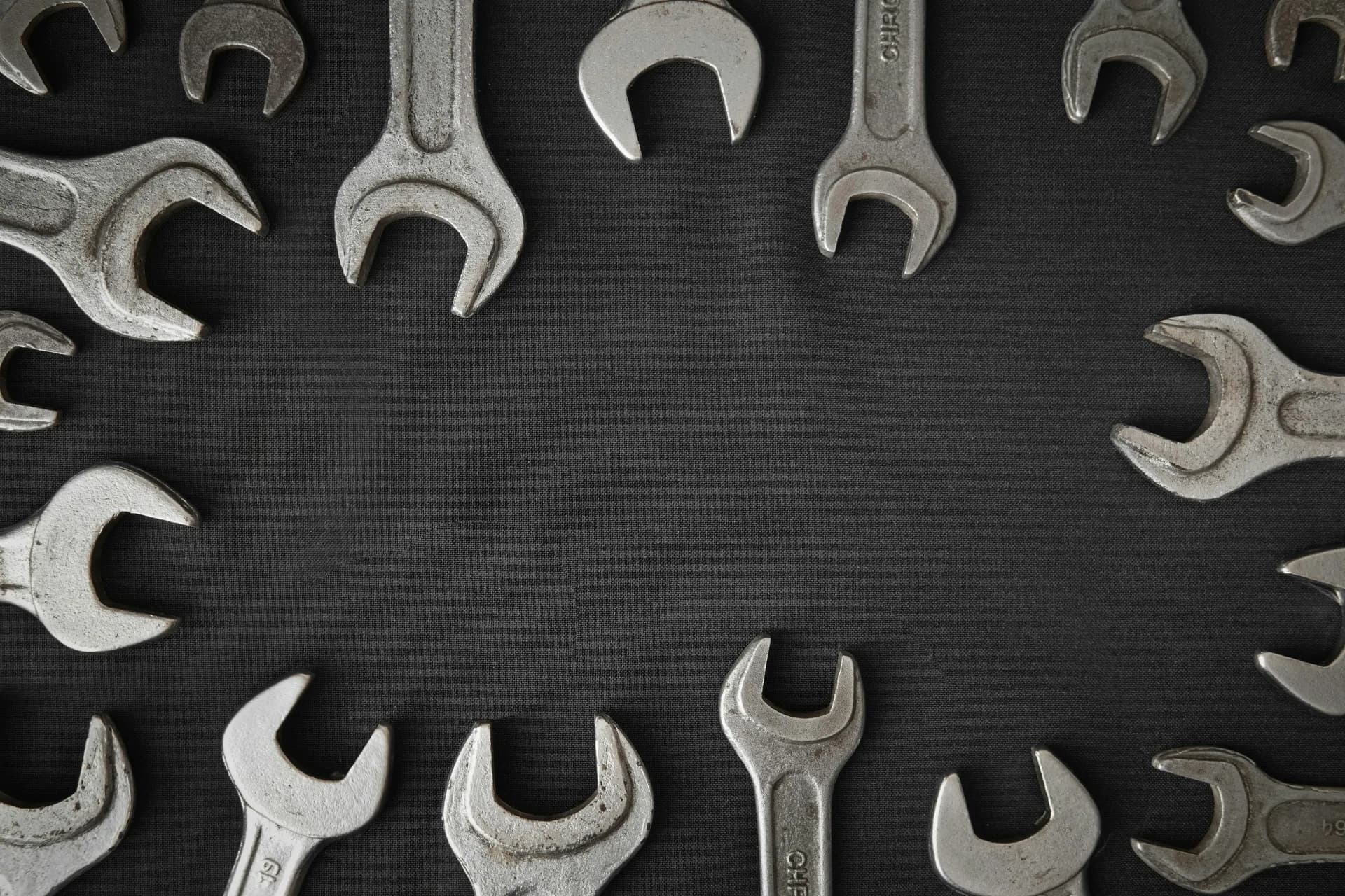 Assortment of worn steel open-end wrenches arranged in a ring around the edges of a dark cloth surface
