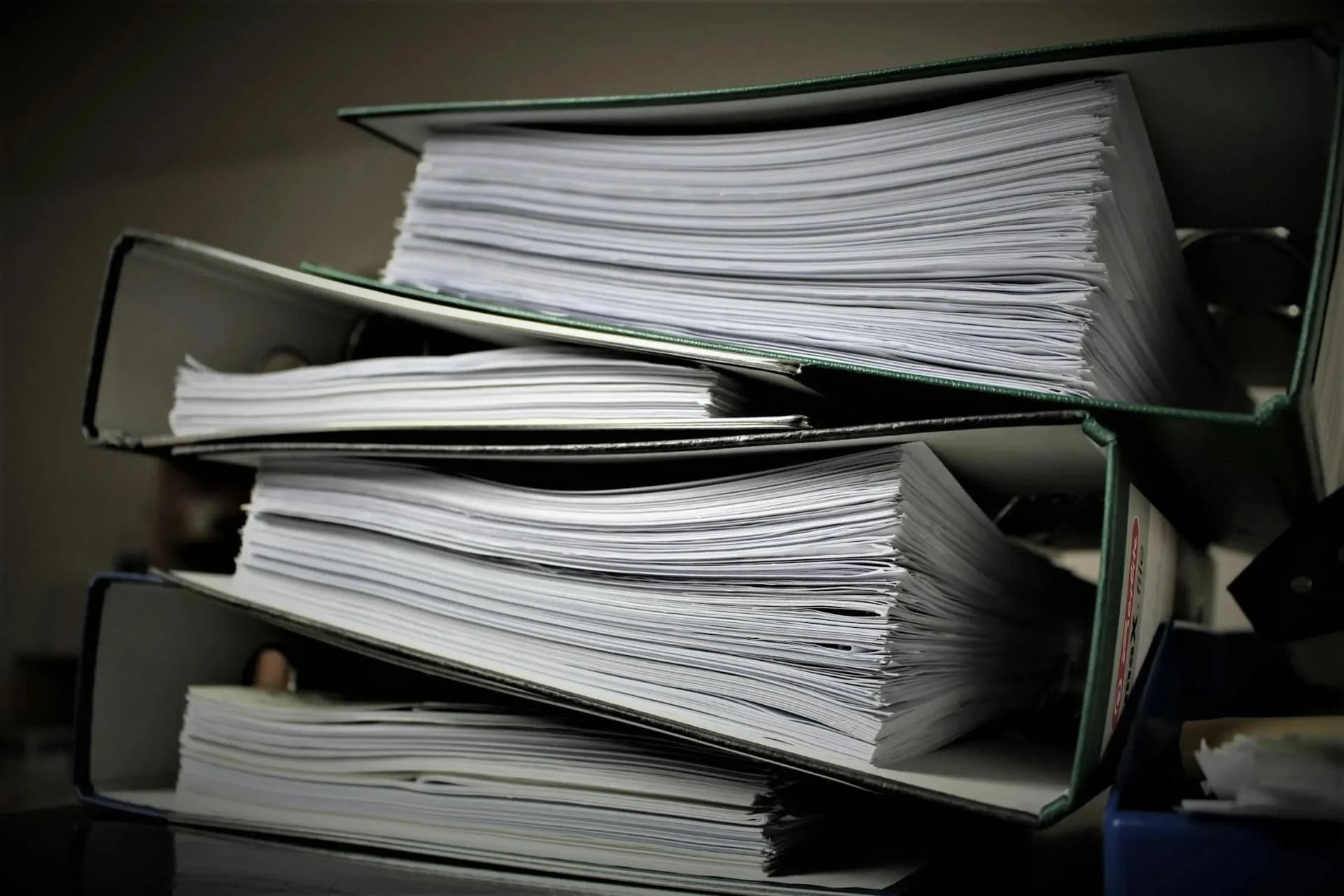 Stack of thick ring binders overflowing with paper documents in a dim office
