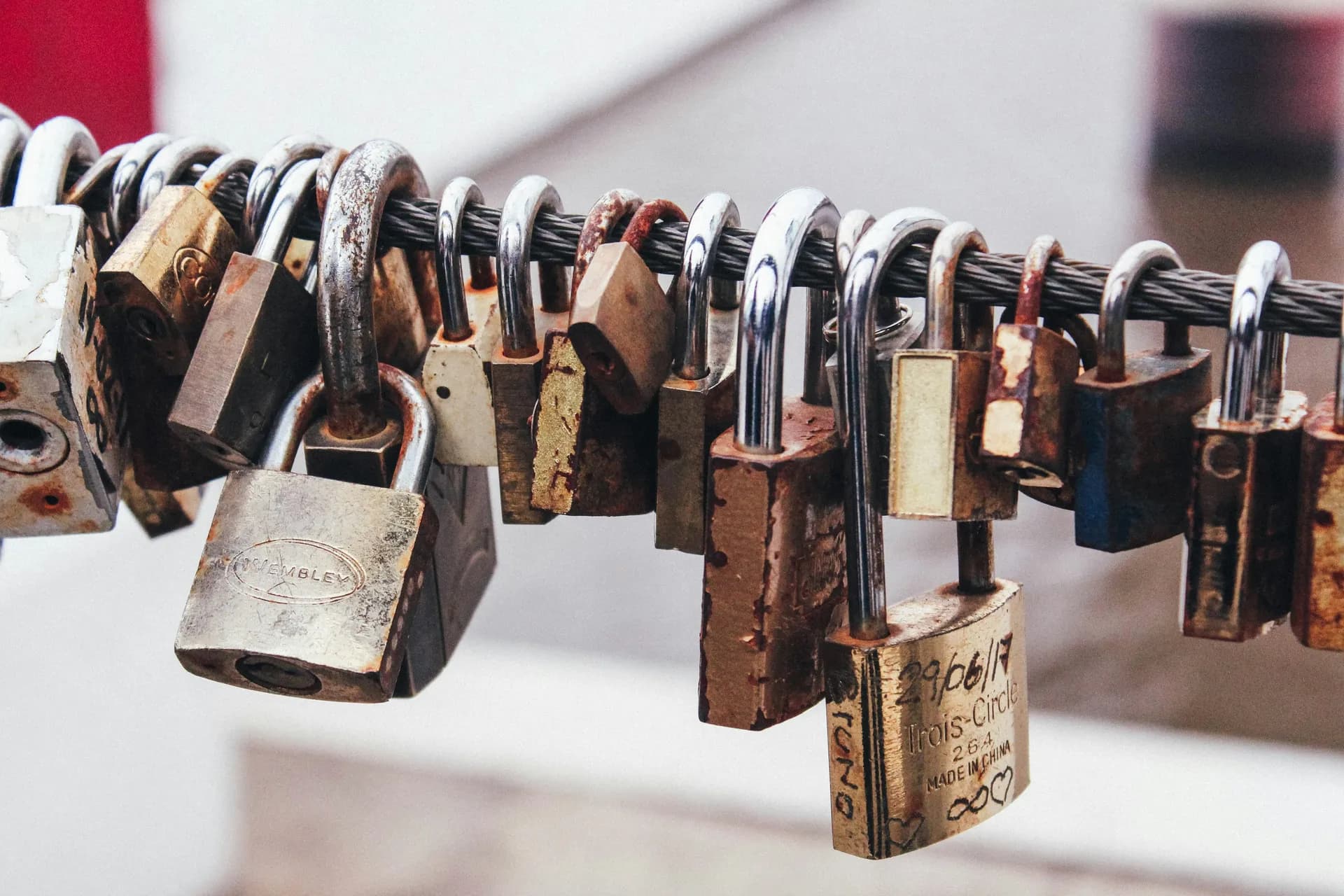Close-up of many weathered and rusty padlocks locked onto a steel cable